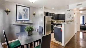 A modern kitchen with a central island, dark cabinetry, and a dining area with a table and chairs. - Chic Dallas Condo w/ Pool, Walk to Knox Street! (Dallas)