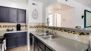A modern kitchen with dark cabinets, a stainless steel countertop, a double sink, and a decorative tiled backsplash. - Chic Dallas Condo w/ Pool, Walk to Knox Street! (Dallas)