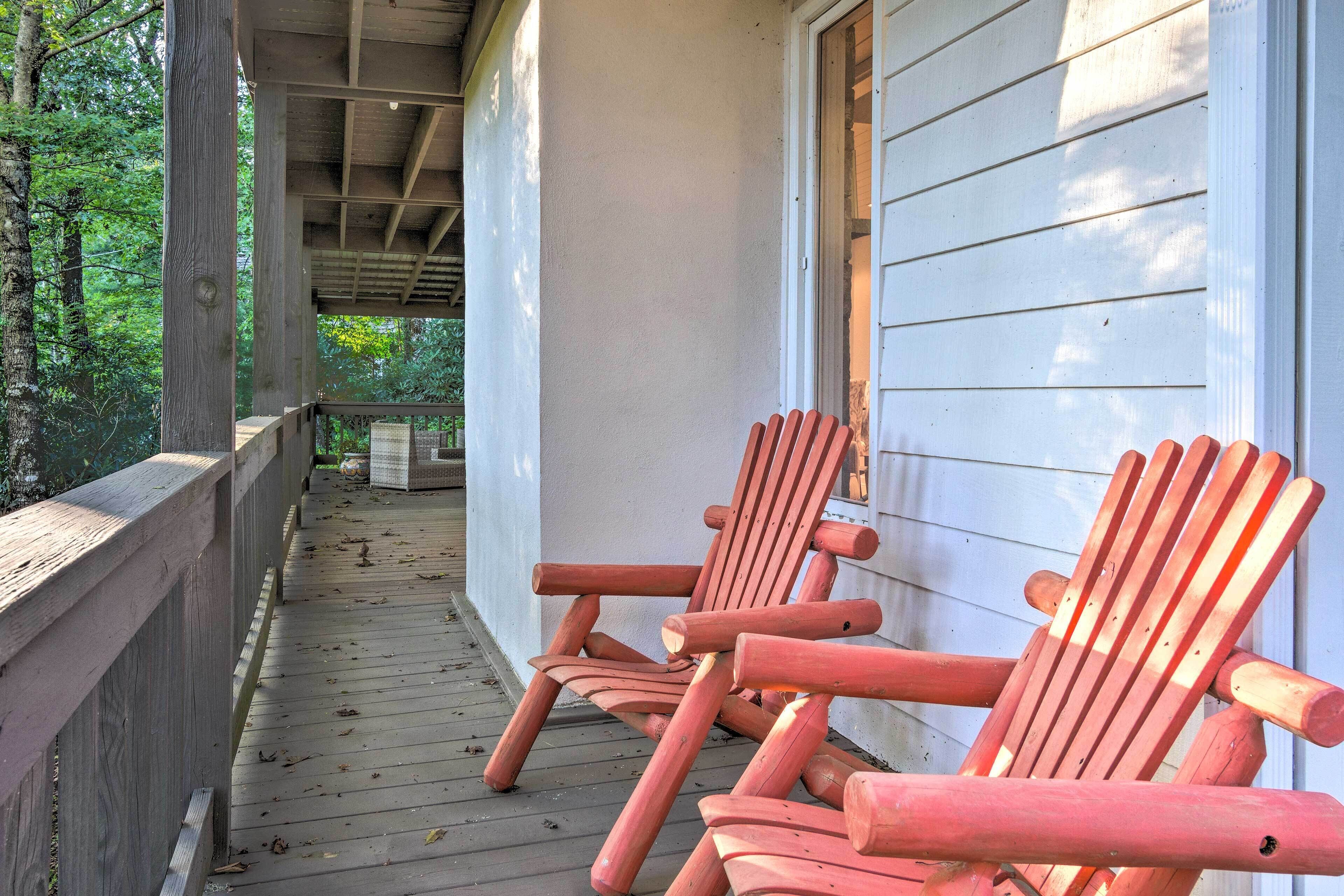 A wooden porch with two Adirondack chairs and a wooden railing.