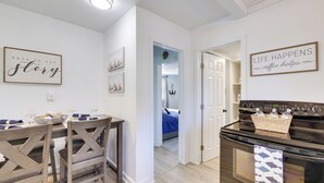 A modern kitchen with a dining table, chairs, and a stove. There are framed signs on the walls and a visible door leading to another room. - Walk to Lake: Nautical Akron Cottage w/ Deck! (Akron)
