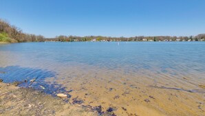 A clear view of a lake with a sandy shore and a distant shoreline with buildings. - Walk to Lake: Nautical Akron Cottage w/ Deck! (Akron)