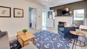 A living room with a blue rug, a fireplace, a TV, and a sofa. - Walk to Lake: Nautical Akron Cottage w/ Deck! (Akron)