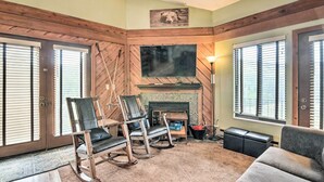 A cozy living room with a fireplace, wooden walls, and a television. - Brian Head Condo w/ Shared Pool & Hot Tub! (Brian Head)