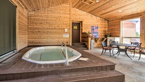 A wooden cabin interior with a hot tub, a dining area with chairs, and a staircase leading to an upper level. - Brian Head Condo w/ Shared Pool & Hot Tub! (Brian Head)