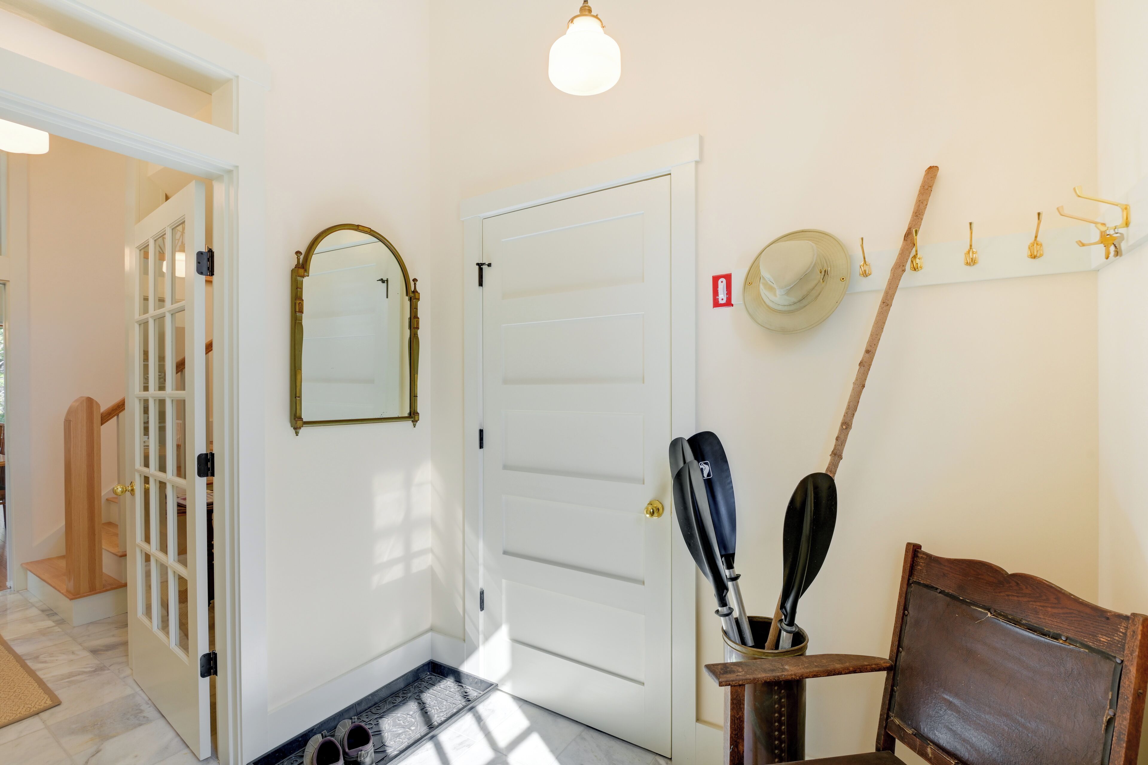 A hallway with a white door, a mirror, a coat rack, and a chair.