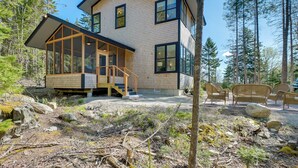 Une maison moderne dotée d’une grande baie vitrée, d’une terrasse en bois et de mobilier d’extérieur.