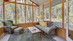 Une pièce chaleureuse avec un plafond en bois, de grandes fenêtres, un canapé, deux fauteuils, une petite table et un tapis à motifs.