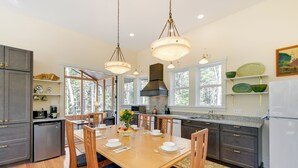 Une cuisine moderne avec une table à manger en bois, des meubles de rangement aux couleurs sombres et une grande fenêtre qui laisse entrer la lumière naturelle.
