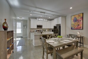 Une cuisine moderne avec des meubles blancs, un îlot central et un coin repas avec une table dressée pour quatre personnes.