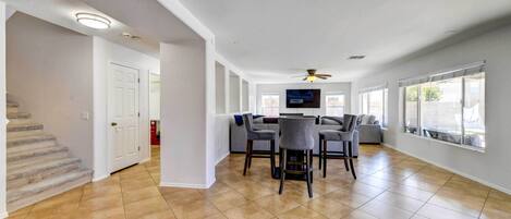 A spacious living area with a dining table and chairs, a ceiling fan, and large windows.