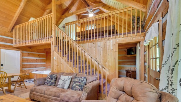 Ein Holzblockhaus-Innenraum mit Sofa, Sesseln und einer Treppe zu einem Schlafboden.