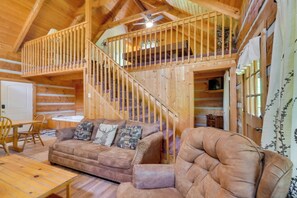 A wooden cabin interior with a sofa, armchair, and a staircase leading to a loft. - Gatlinburg Cabin w/ Pool Table ~ 6 Mi to Downtown! (Gatlinburg)