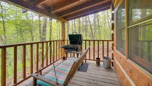 Eine Holzterrasse mit einer Schaukel, einem Grill und Blick auf den Wald.