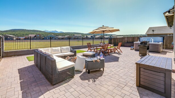 An outdoor patio with wicker furniture, a grill, and a view of a sports field. - Spacious Bellemont Cabin w/ Jacuzzi + Mtn View! (Bellemont)