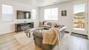 A spacious living room with a fireplace, a sofa, a television, and a door leading to a balcony. - Spacious Bellemont Cabin w/ Jacuzzi + Mtn View! (Bellemont)