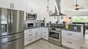 Uma cozinha moderna com eletrodomésticos de aço inoxidável, armários brancos e painel de parede revestido com azulejos.