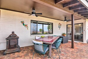 An outdoor patio with a brick floor, a table with chairs, a ceiling fan, and decorative wall hangings. - Lake Powell Views: Mid-century Home in Page (Page)