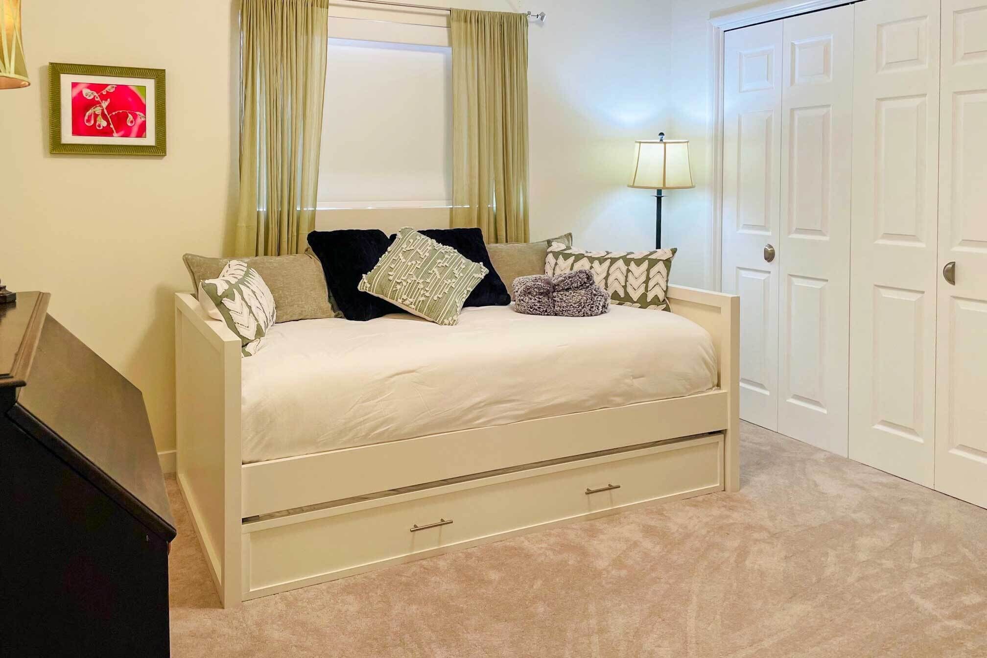 A bedroom with a bed, a nightstand, a lamp, a door, and a framed picture on the wall.