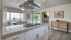 A modern kitchen with a large island, white cabinetry, and a stainless steel range hood.