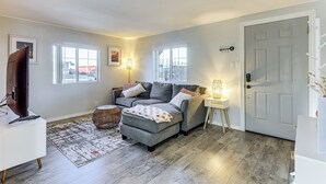A living room with a grey sofa, a white side table, a wicker ottoman, and a patterned rug. - Updated Escape w/ Game Room 1 Block to River! (Bullhead City)