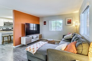 A living room with a sofa, TV, and a kitchen area with a microwave. - Updated Escape w/ Game Room 1 Block to River! (Bullhead City)