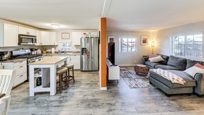A modern kitchen with a central island, stainless steel appliances, and a dining area with a sofa and coffee table. - Updated Escape w/ Game Room 1 Block to River! (Bullhead City)
