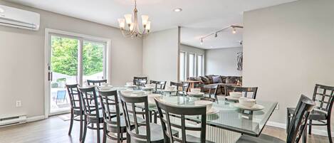 A spacious dining area with a glass-top table and dark chairs, a chandelier, and a view of the outdoors.