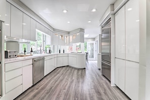 A modern kitchen with white cabinetry, stainless steel appliances, and a wooden floor.