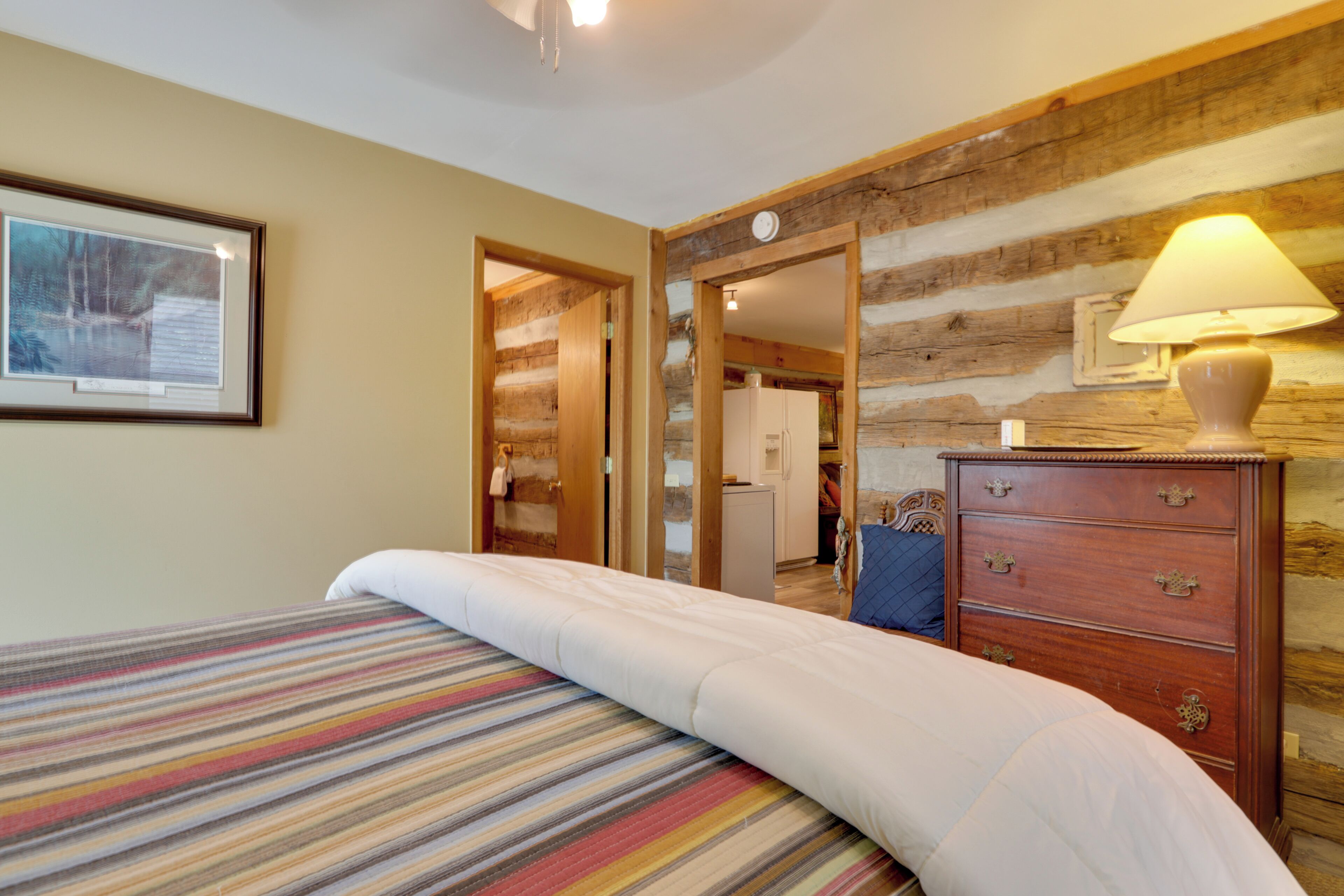 Une chambre d’hôtel avec un lit, une commode en bois, une lampe et un tableau encadré au mur.