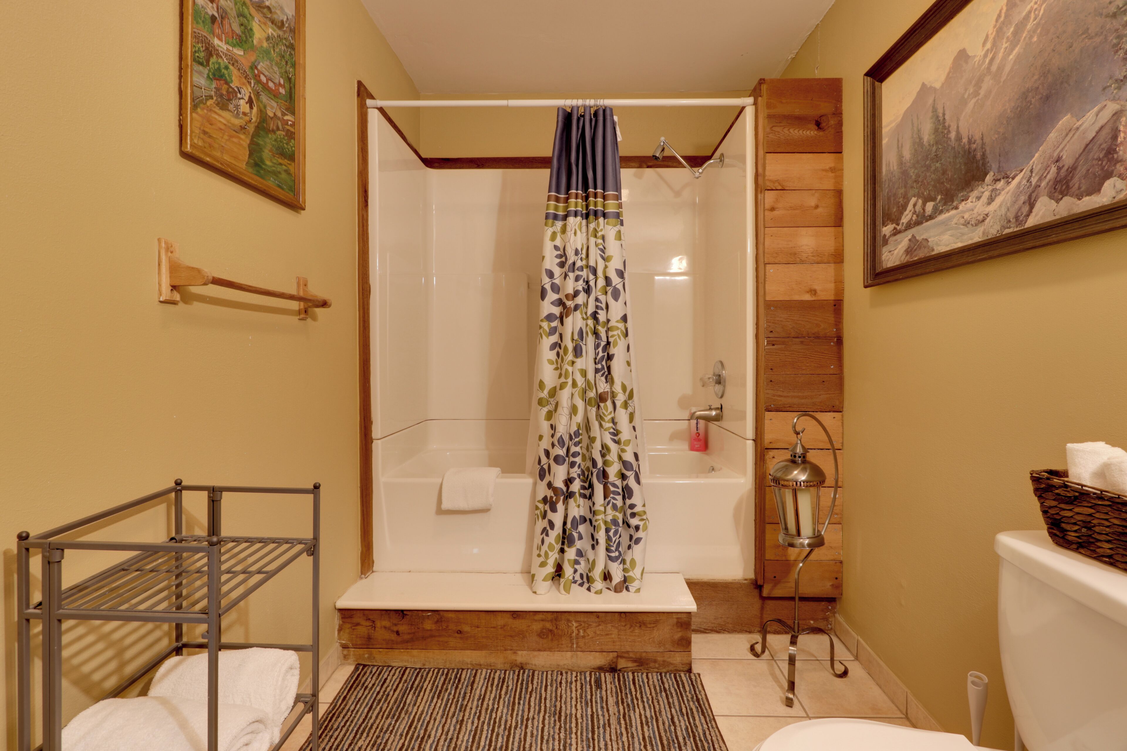 A bathroom with a shower, a bathtub, a toilet, a sink, a towel rack, a shelf, and a painting on the wall.