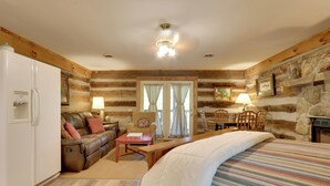 A cozy room with a bed, a wooden dining table, a sofa, and a refrigerator. - Fire Pit & Deck! Cozy Smoky Mtn Retreat on River (Townsend)