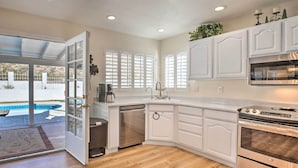 Una cocina con muebles blancos, lavavajillas, horno y vista a una piscina a través de un ventanal.