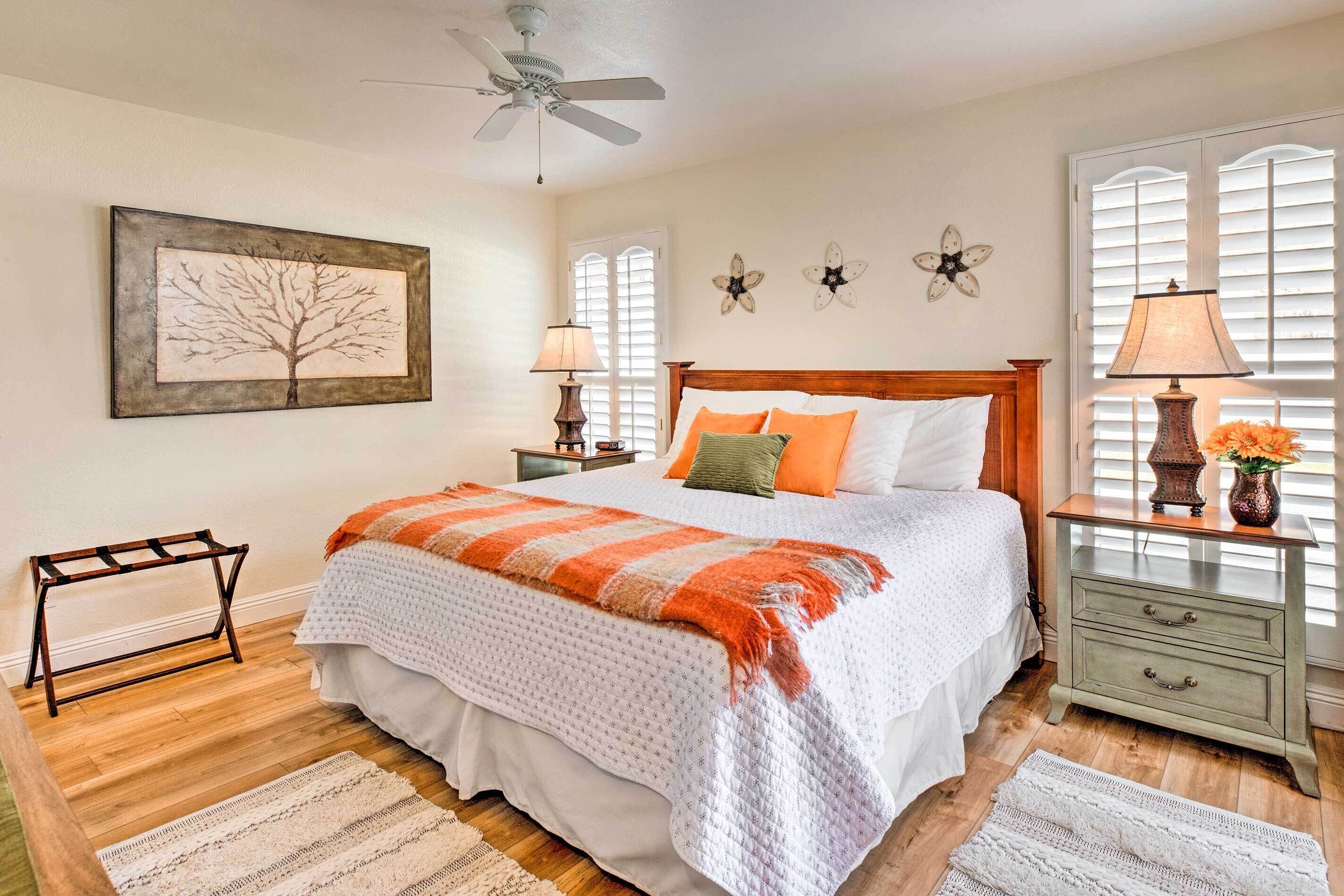 A bedroom with a bed, nightstands, a wooden floor, a ceiling fan, and a window with blinds.