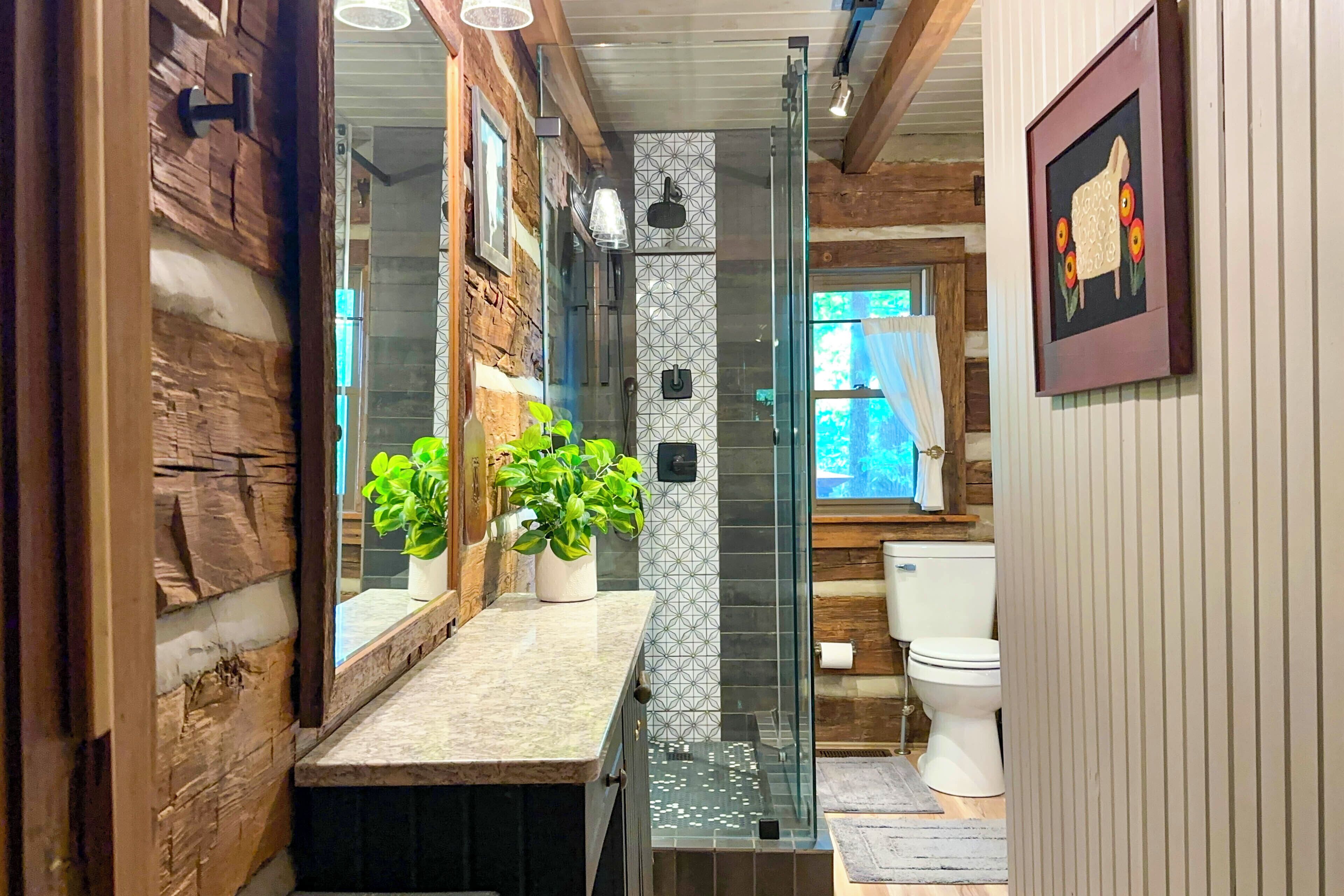 A bathroom with a glass shower enclosure, wooden walls, a marble countertop, and a toilet.