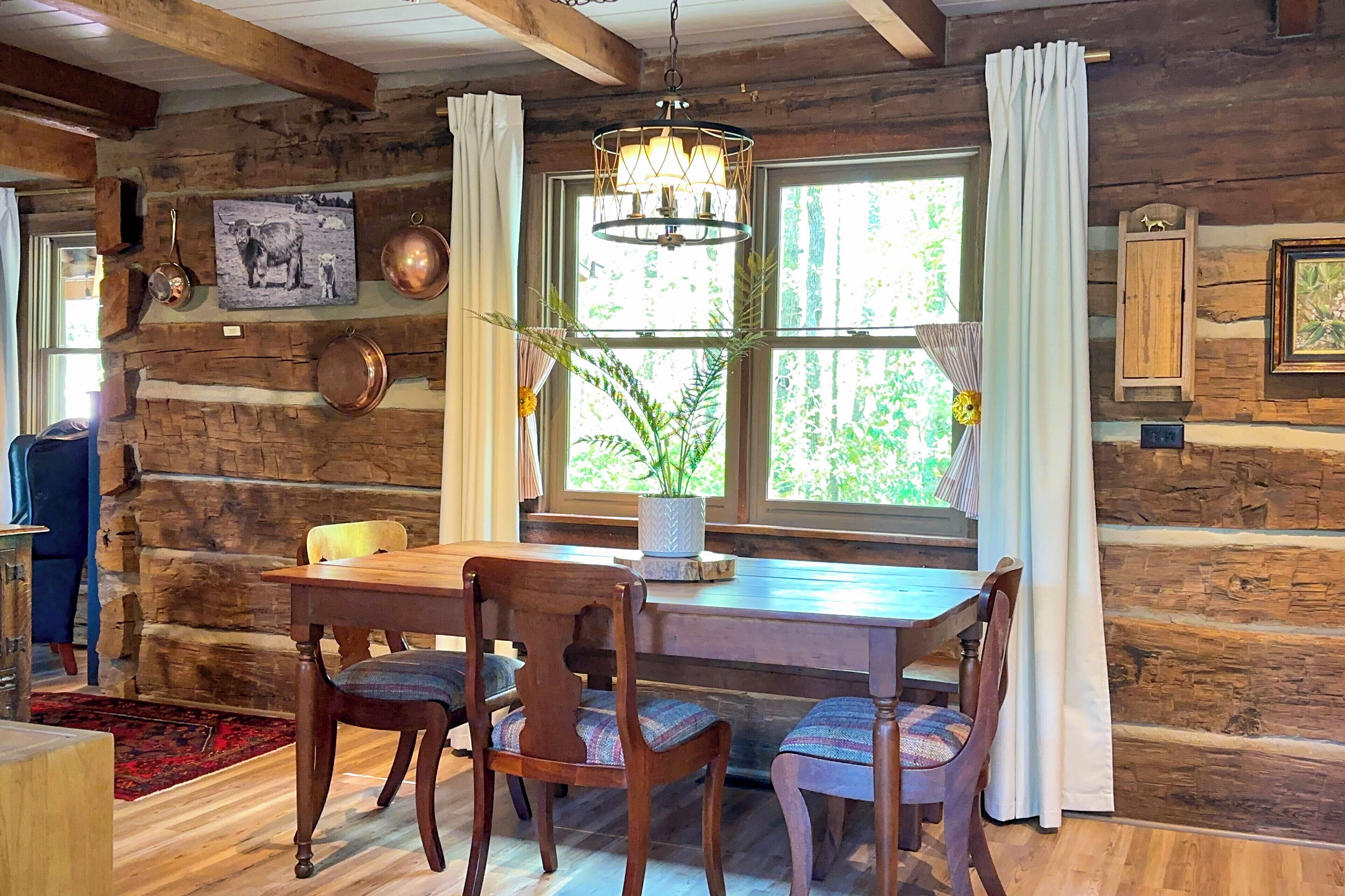 A rustic wooden interior with a dining table, chairs, a chandelier, and a window with curtains.