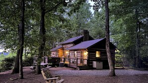 A rustic cabin with a fire pit, wooden deck, and a stone chimney.