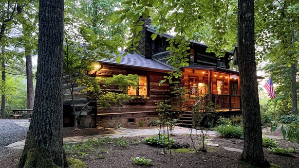 A rustic log cabin with a porch, surrounded by trees and a garden.