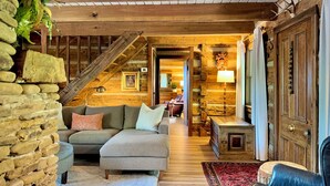 A cozy interior with a stone wall, wooden staircase, a sofa, and a lamp.