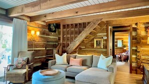 A log cabin interior with a sofa, armchair, ottoman, and a staircase.