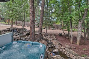 Un bain à remous situé dans un espace boisé, avec un petit ruisseau et une clôture en bois.