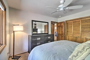Une chambre à coucher comprenant un lit, une commode, un miroir, un ventilateur de plafond et des placards en bois.