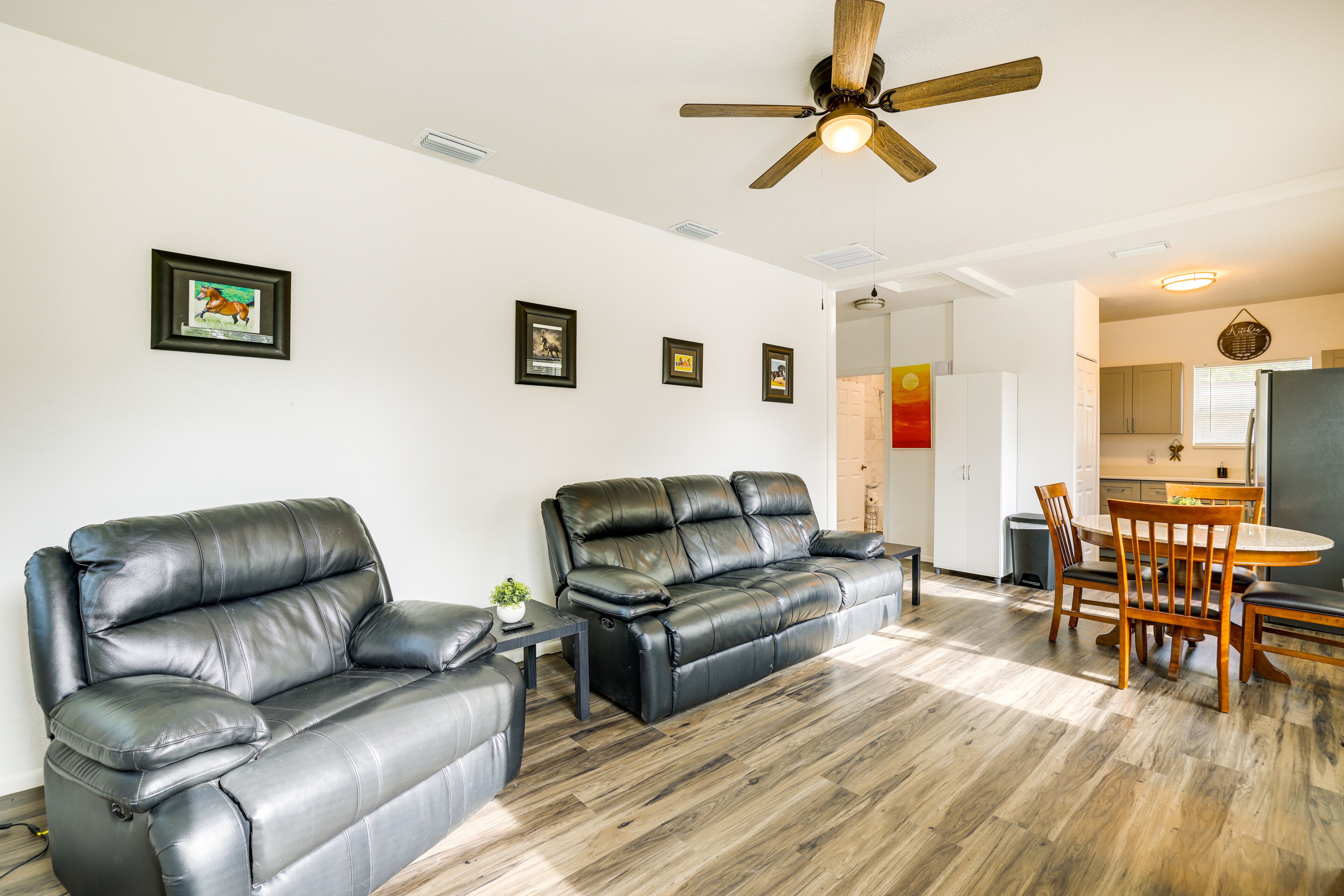 A modern living room with a black leather sofa, a wooden dining table with chairs, and a ceiling fan.