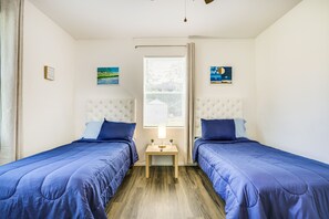 A bedroom with two beds, a nightstand, a window with blinds, and two wall-mounted paintings. - Ocala Vacation Rental in Downtown w/ Covered Patio (Ocala)