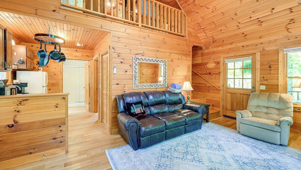 A wooden cabin interior with a dining area, a sofa, a chair, and a large mirror. - Charming Cabin w/ Wraparound Deck in Blue Ridge! (Sparta)