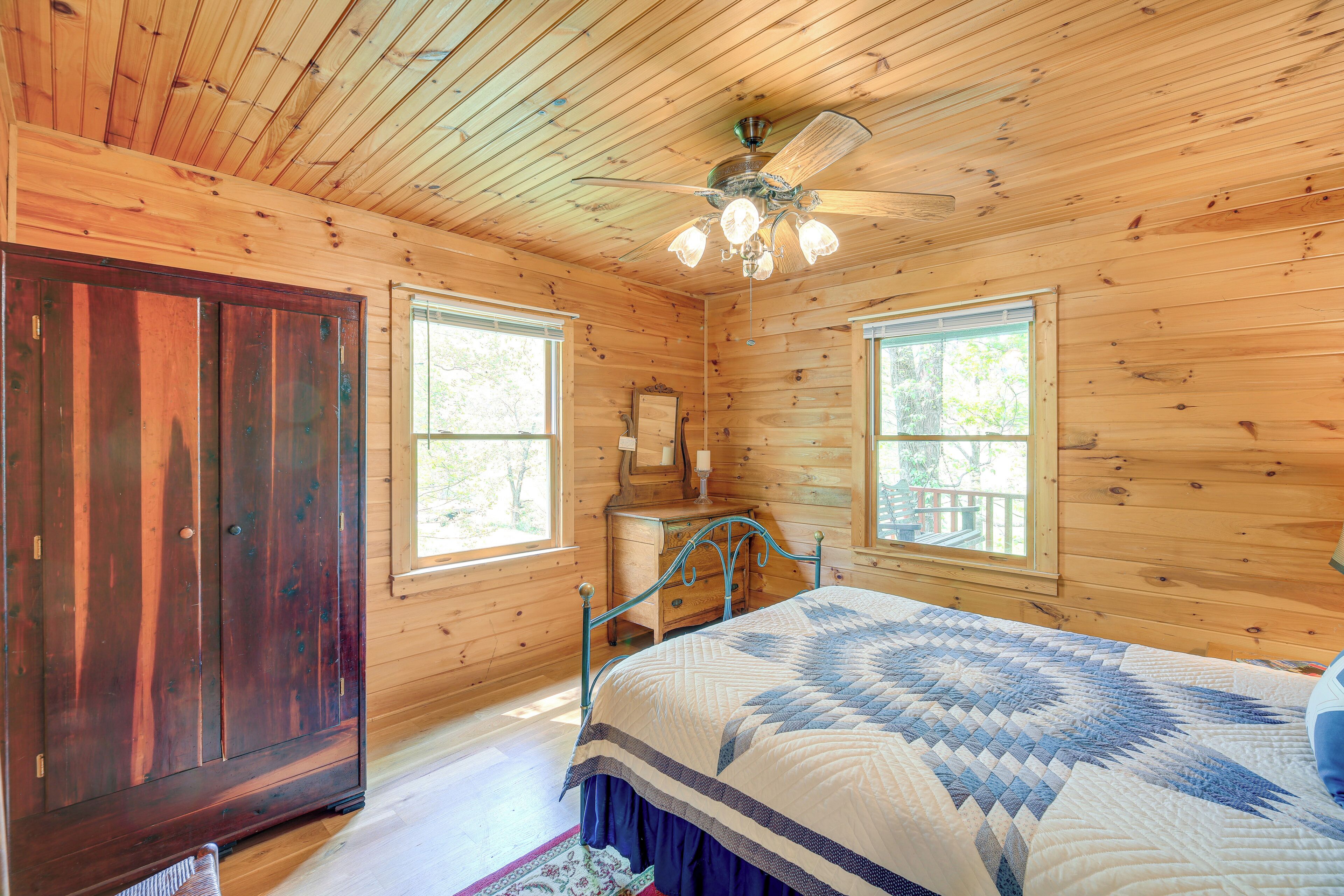 Dormitorio de cabaña de madera con cama, cómoda y ventilador de techo.