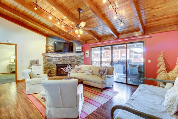 A spacious living room with a stone fireplace, wooden ceiling beams, and a large sliding glass door leading to an outdoor area.