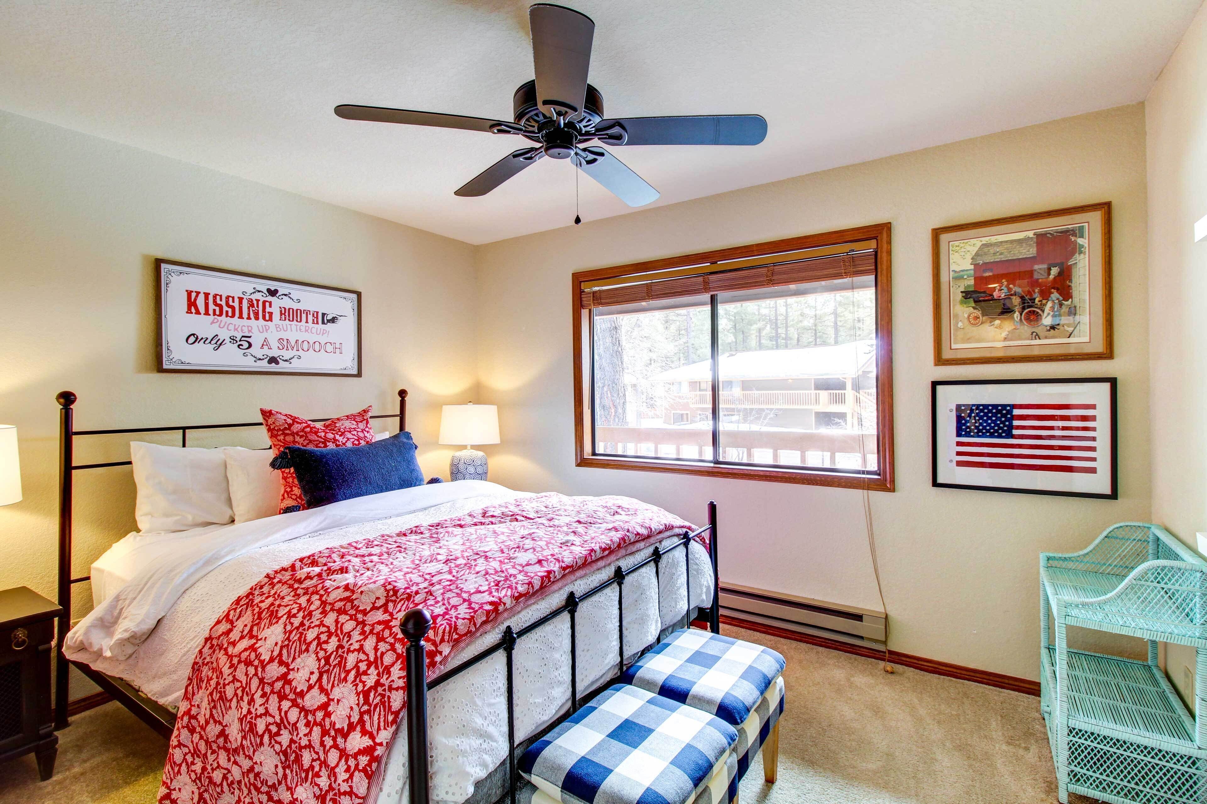 A bedroom with a bed, a ceiling fan, a window with blinds, and a framed American flag.