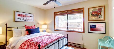A bedroom with a bed, a ceiling fan, a window with blinds, and a framed American flag.