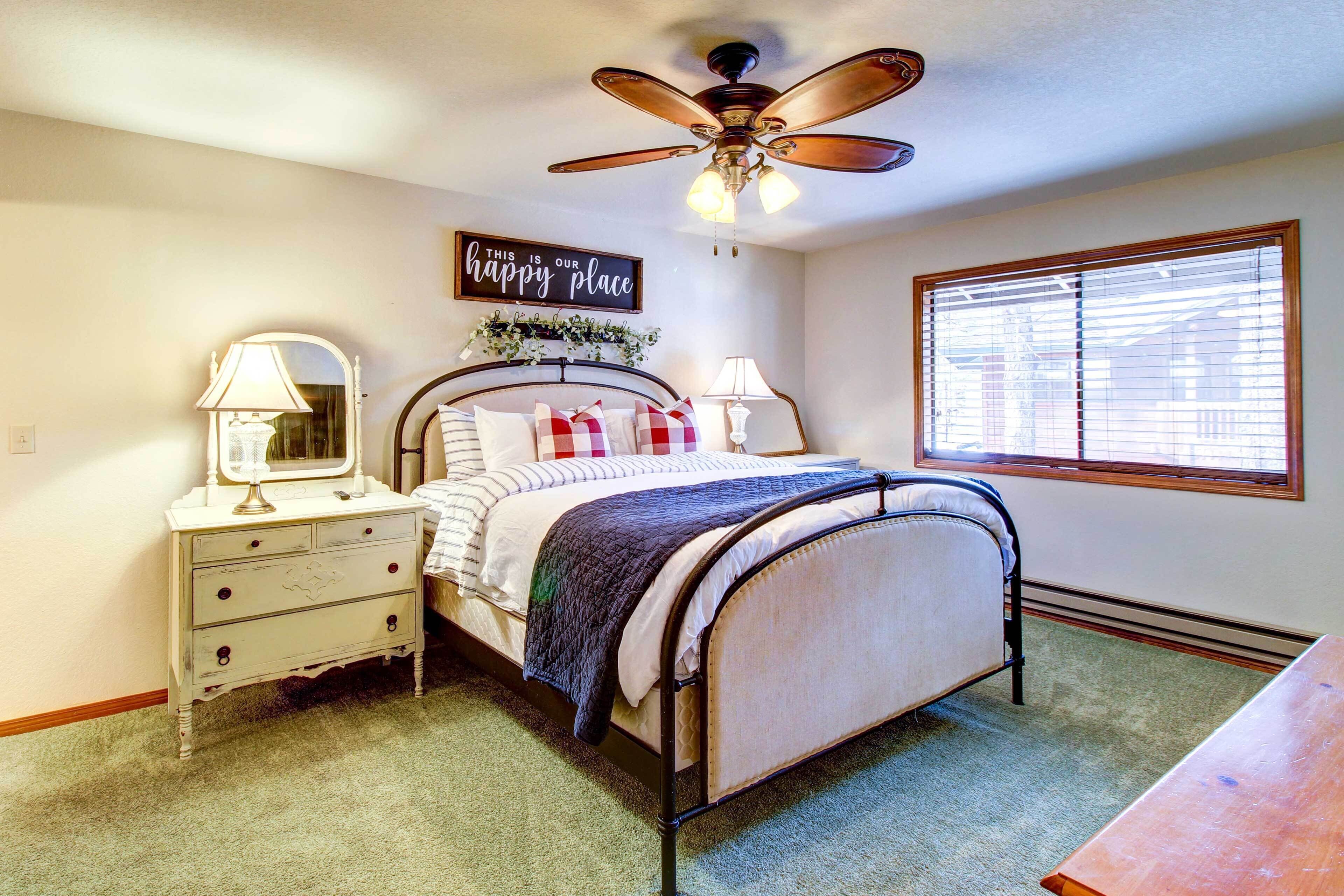 A bedroom with a bed, bedside tables, a ceiling fan, a window with blinds, and a sign on the wall.