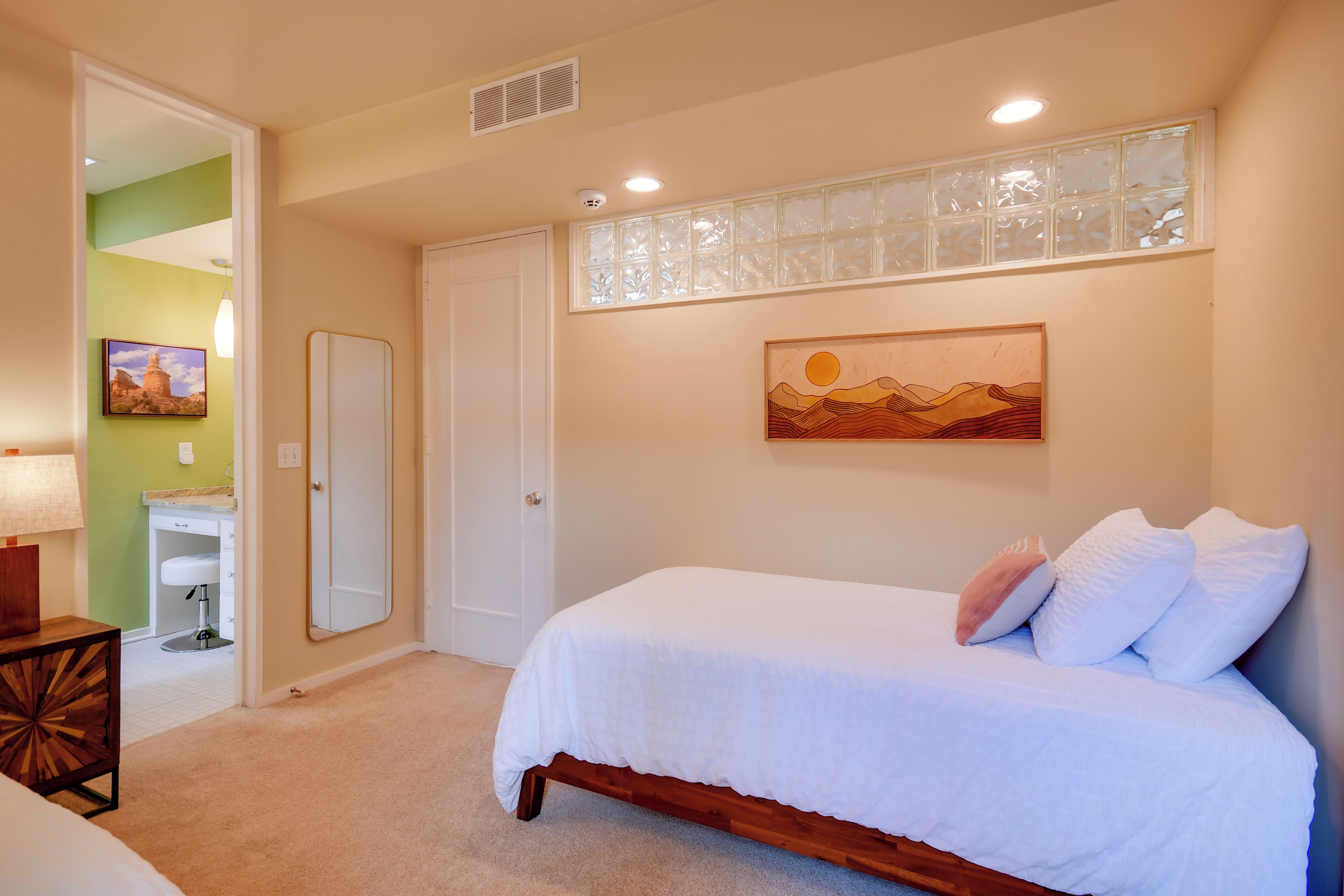 A bedroom with a bed, a nightstand, a lamp, a bathroom with a sink, and a door.
